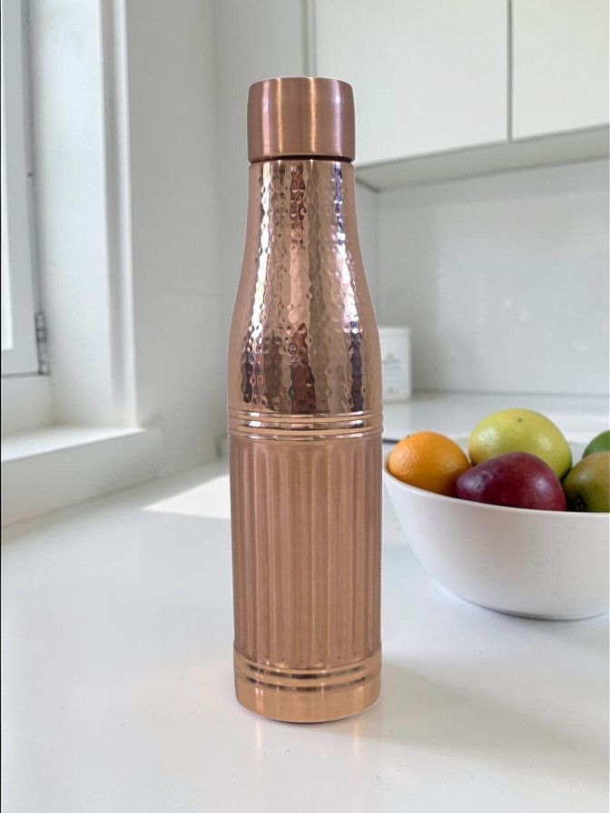 Copper water bottle on a kitchen counter with fruit in the background