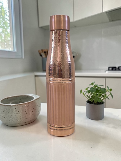 Rose gold water bottle on a kitchen counter with plants and a window in the background