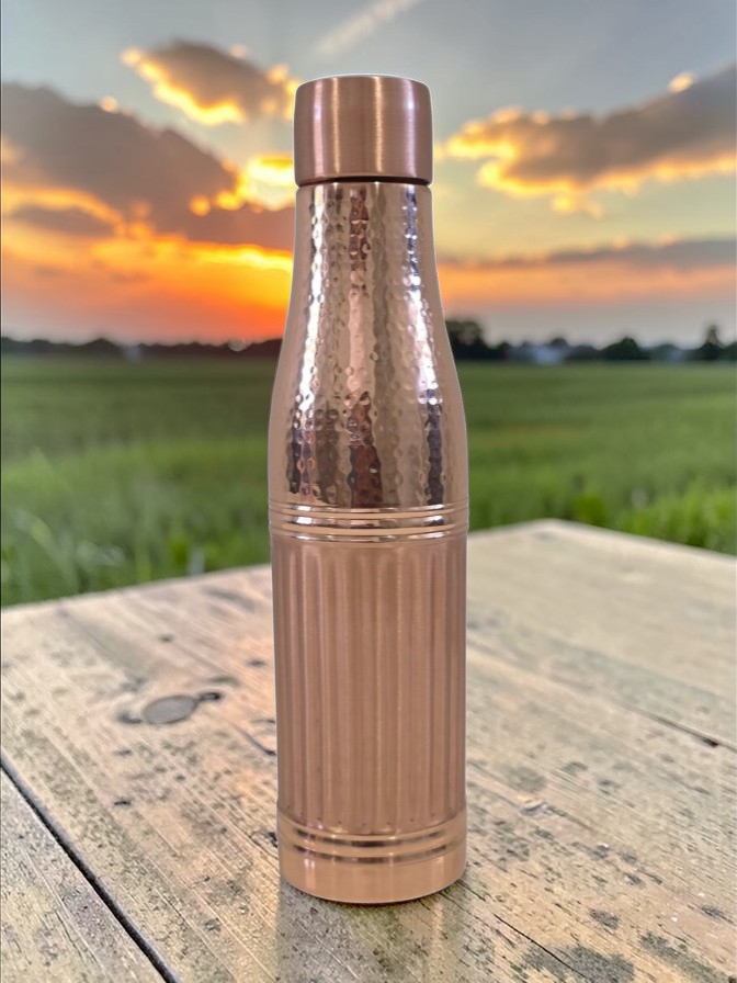 Rose gold water bottle on a wooden surface with a sunset in the background