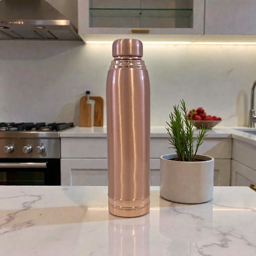Rose gold water bottle on a kitchen counter with a plant and fruit bowl in the background