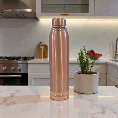 Rose gold water bottle on a kitchen counter with a plant and fruit bowl in the background